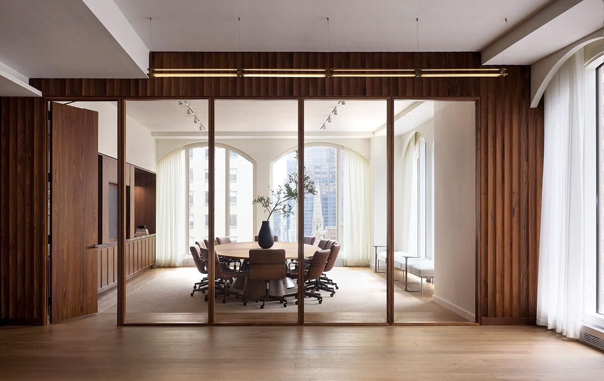 A boardroom with a round table, seen through glass walls and wood paneling